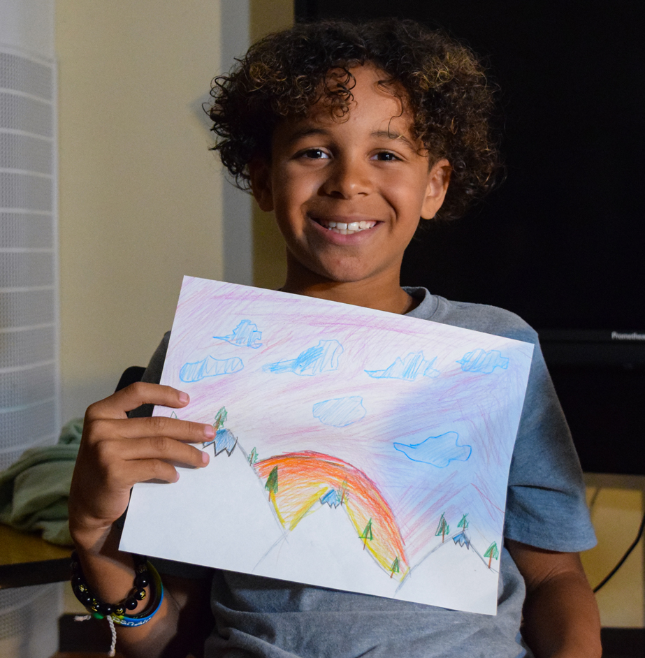 Young student smiling and holding a piece of their artwork.